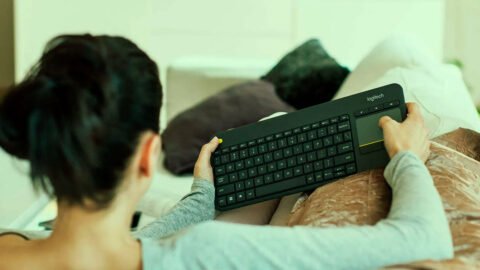 Teclado inalámbrico Logitech K400 Plus sobre una mesa frente a una TV encendida.